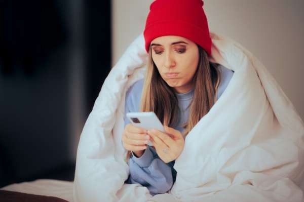 Woman wrapped in blanket holding cell phone.