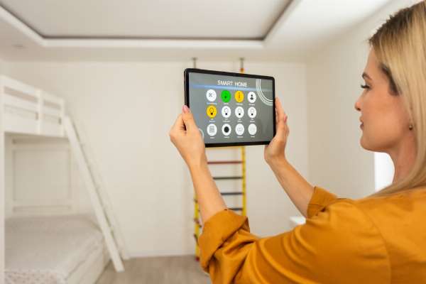 A woman holding up a tablet displaying a smart home management screen