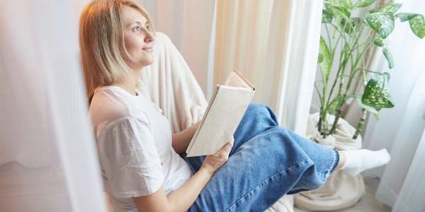 A woman holding a book smiling as she looks into the distance in this image from Shutterstock
