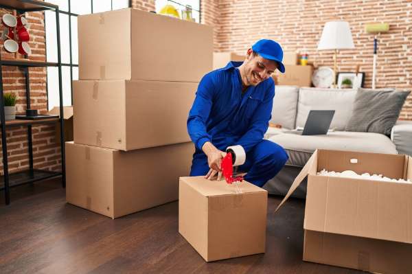A man taping up a cardboard box in a living room in this image from Shutterstock