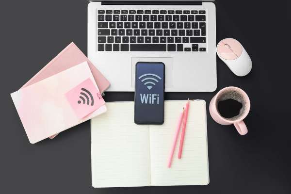 A phone, laptop, notebook, coffee, and pen, with ‘WiFi’ written on the phone screen in this image from Shutterstock