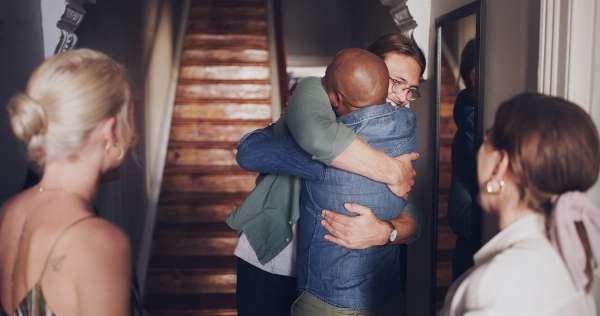 A young man embracing a friend at the entryway of a home in this image from Shutterstock