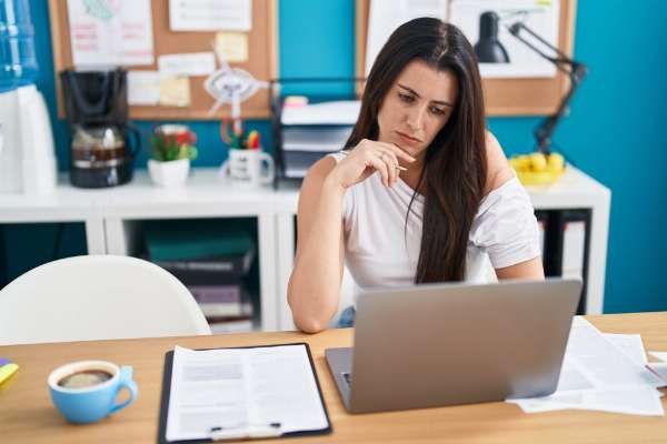 Woman sitting at a desk and staring pensively into her laptop in this image from Shutterstock 