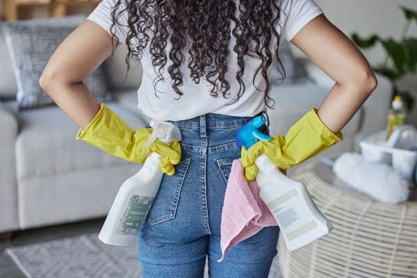 A woman stands with her back to the camera wearing rubber gloves and holding two bottles of cleaning solution in this image from Shutterstock